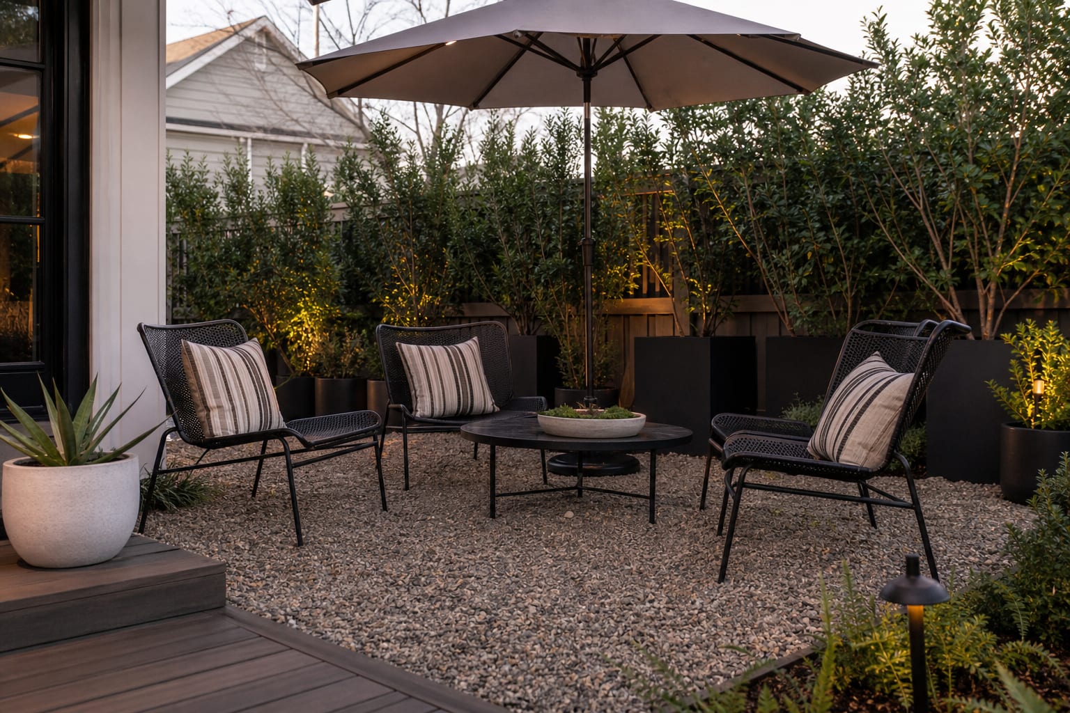 budget backyard seating zone with pea gravel, black metal chairs, large umbrella, and planters used as a privacy edge