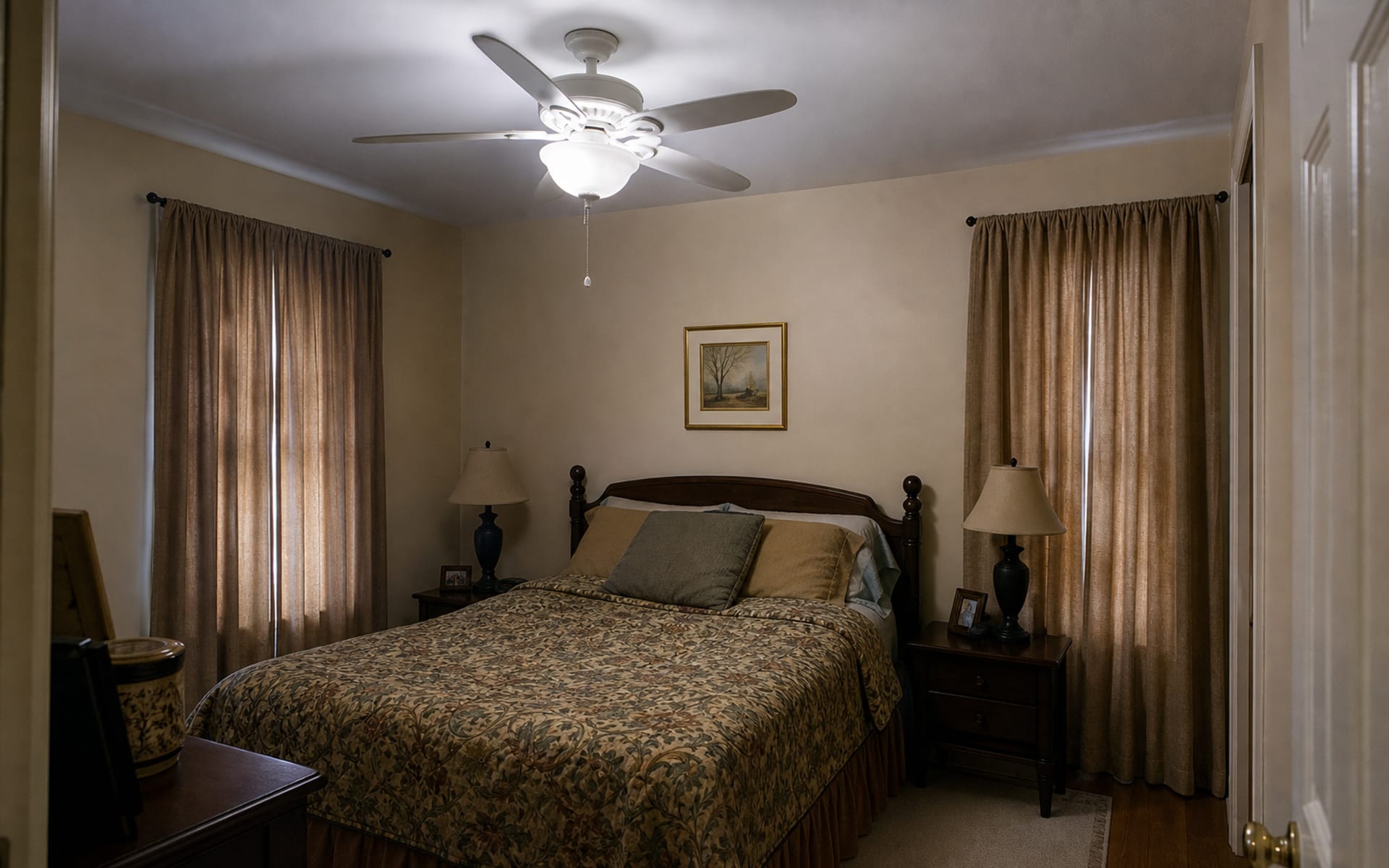 Small bedroom with a flat white ceiling, dated ceiling fan, beige walls, heavy curtains, and mismatched bedding.