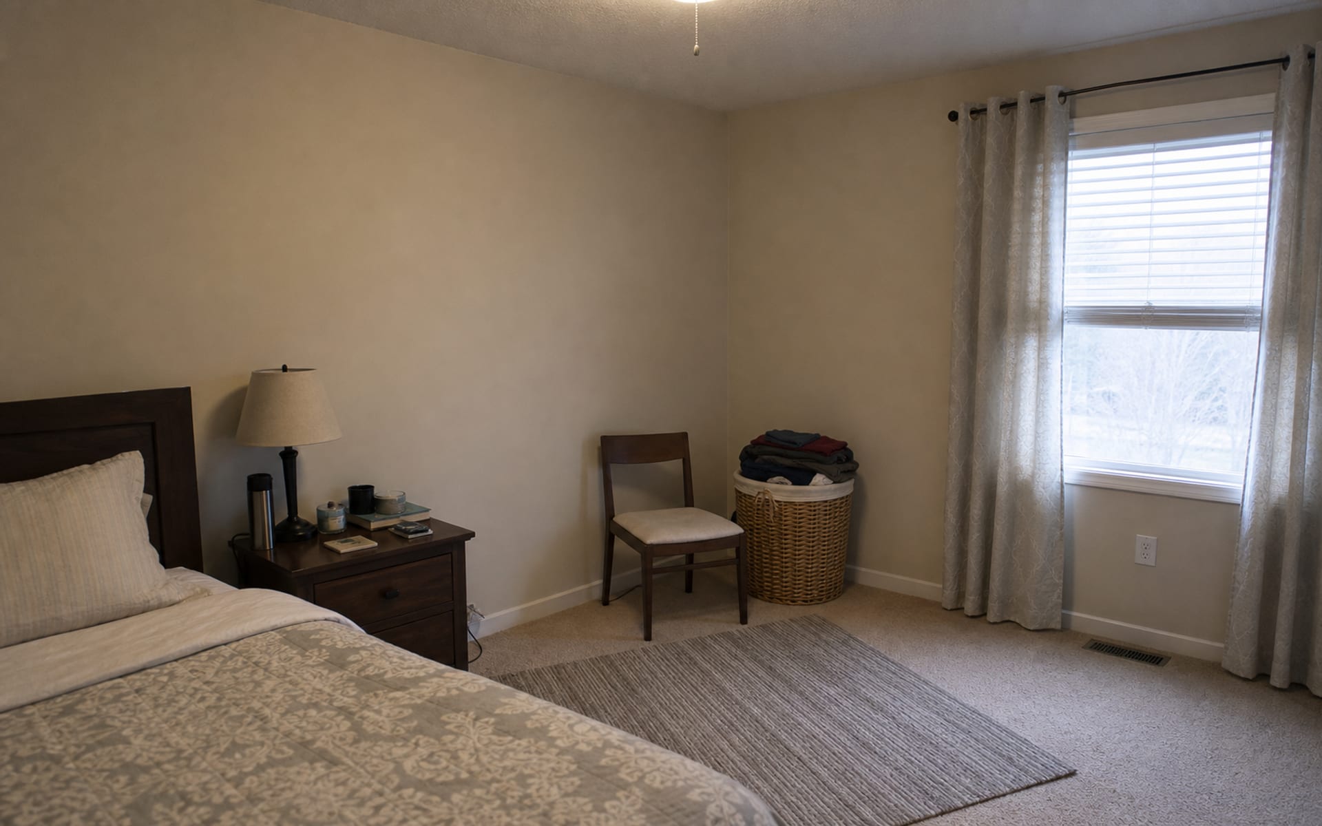 Bedroom corner with a laundry basket, unused accent chair, no side table, and cold overhead light.