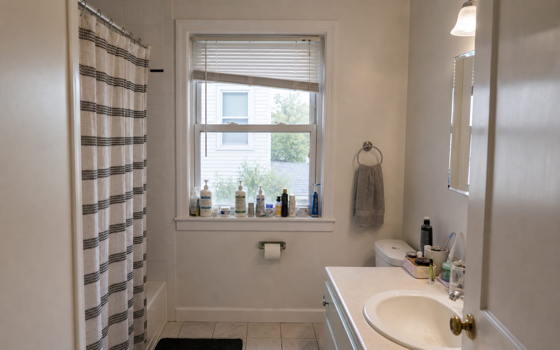 Small bathroom with a bare double-hung window, exposed lower sash, cluttered sill, and harsh overhead light.
